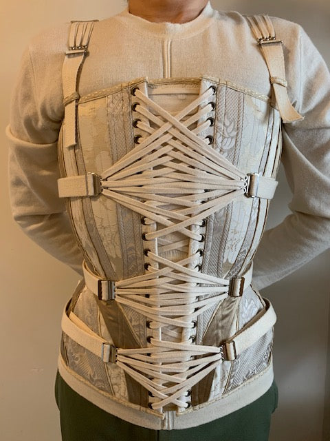 Close up of a man's torso wearing an ivory corset with three pairs of front fan lacing straps