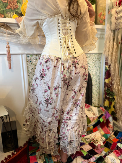 Person wearing a floral outfit with the ivory satin  cincher corset in a decorative room.